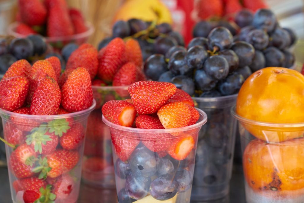 Vibrant strawberries, grapes, and persimmons displayed in plastic cups at a market.